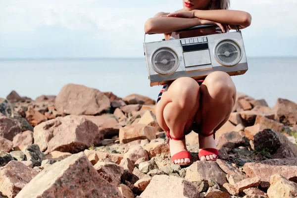 Vue recadrée de la femme élégante posant avec boombox rétro sur la plage rocheuse — Photo de stock