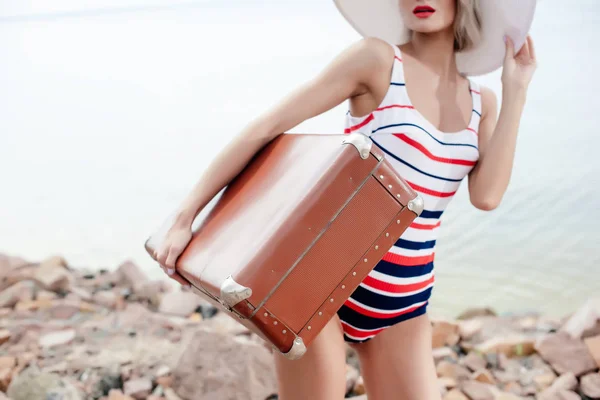 Cropped view of stylish tourist in retro swimsuit holding travel bag — Stock Photo
