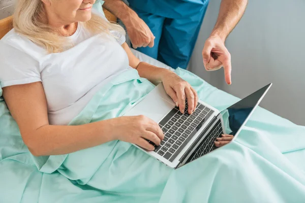 Cropped shot of senior woman using laptop with blank screen in hospital bed — Stock Photo