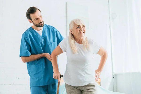 Enfermera masculina que apoya a la mujer mayor con bastón - foto de stock