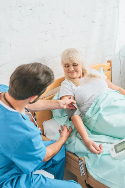 Young doctor measuring blood pressure to senior woman in hospital bed — Stock Photo