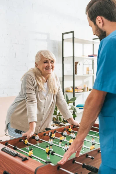 Sorridente donna anziana che gioca a calcio balilla con l'assistente sociale — Foto stock