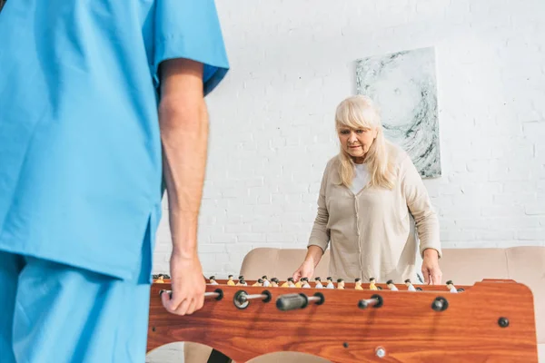 Cropped shot of male nurse and senior woman playing table football — Stock Photo