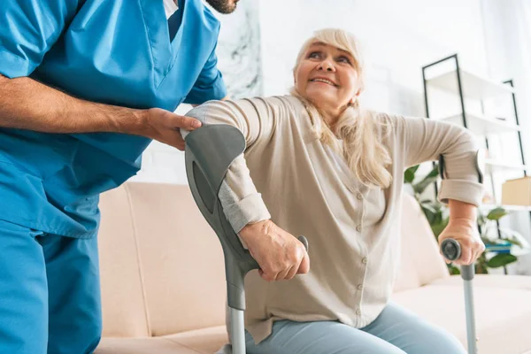 Cropped shot of social worker helping senior woman with crutches — Stock Photo