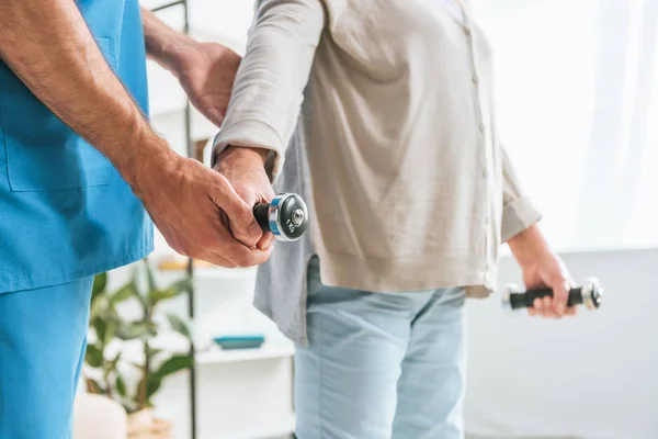 Cropped shot of social worker helping senior woman training with dumbbells — Stock Photo