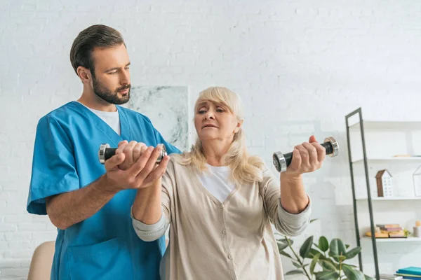 Junge männliche Krankenschwester hilft Seniorin beim Training mit Hanteln — Stockfoto