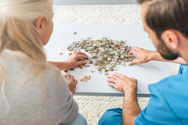 Plan recadré de femme âgée et jeune soignant jouant avec des pièces de puzzle — Photo de stock