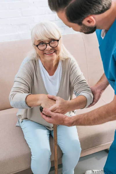 Cropped shot of male nurse supporting smiling senior woman with walking stick — Stock Photo