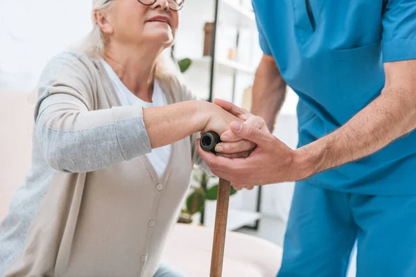 Colpo ritagliato di infermiera maschile aiutare la donna anziana con bastone da passeggio — Foto stock