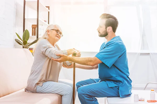 Вид сбоку медсестры-мужчины, поддерживающей пожилую женщину тростью — стоковое фото