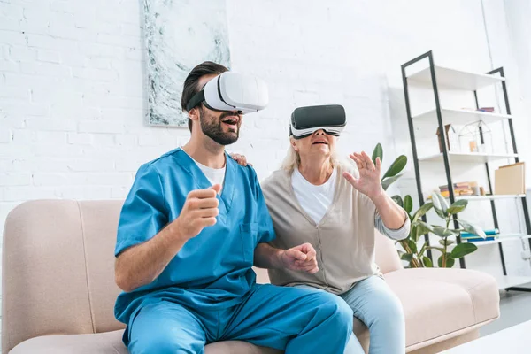 Счастливая старшая женщина и молодой медбрат с помощью наушников виртуальной реальности — стоковое фото
