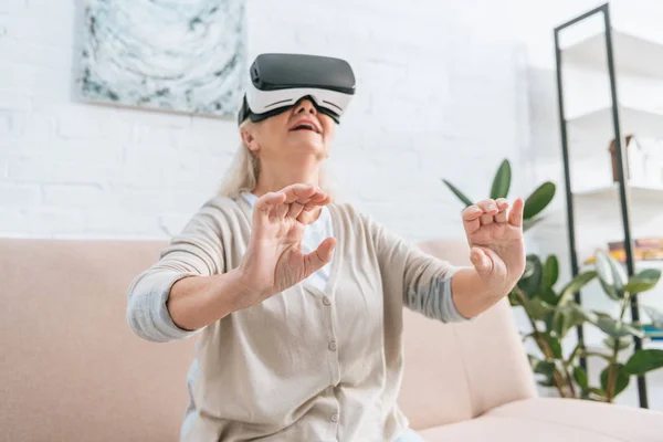 Vue à faible angle de sourire femme âgée en utilisant un casque de réalité virtuelle à la maison — Photo de stock