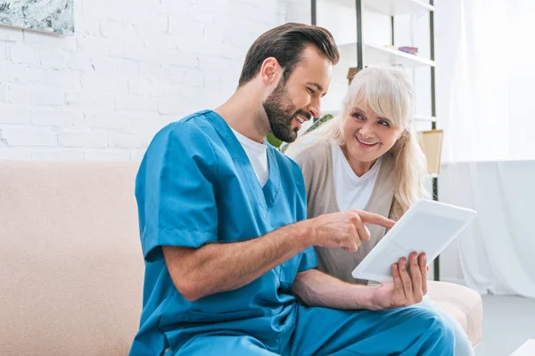 Happy young caregiver and senior woman using digital tablet together — Stock Photo