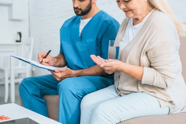 Schnappschuss von Seniorin, die Medikamente nimmt und Krankenschwester, die auf Klemmbrett schreibt — Stockfoto