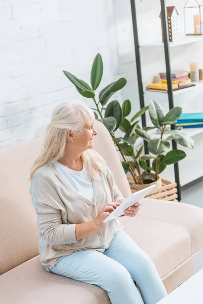 High angle view of smiling senior woman using digital tablet while sitting on couch — Stock Photo