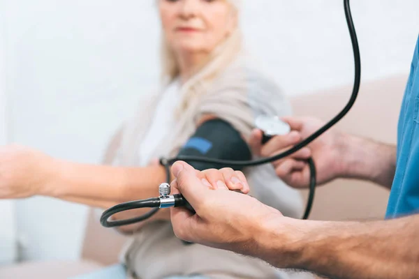 Primer plano vista parcial de la enfermera midiendo la presión arterial a la mujer mayor - foto de stock