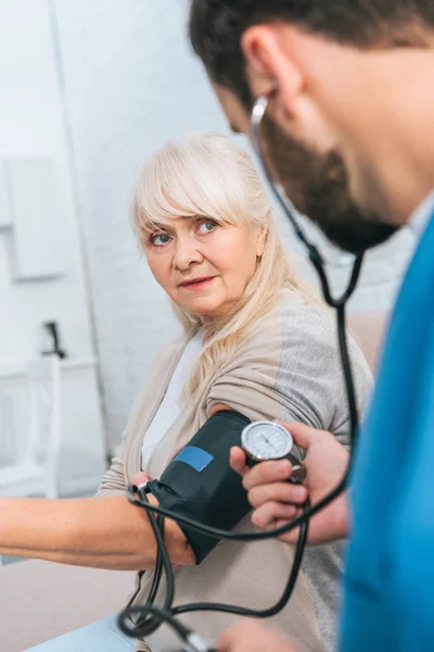 Concentrazione selettiva dell'assistente sociale che misura la pressione sanguigna alla donna anziana — Foto stock