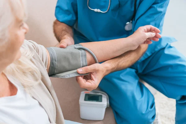 Обрізаний знімок доглядальника, що вимірює кров'яний тиск для старшої жінки — стокове фото