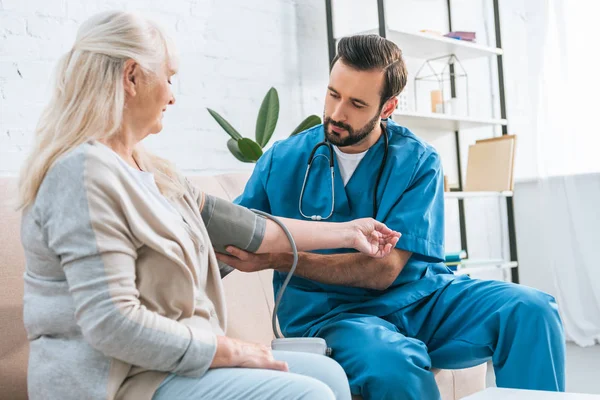 Young male nurse measuring blood pressure to senior woman — Stock Photo
