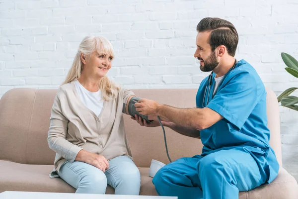 Enfermera masculina sonriente midiendo la presión arterial a la mujer mayor - foto de stock