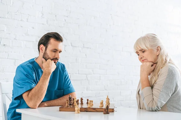 Concentrated senior woman and young social worker playing chess together — Stock Photo