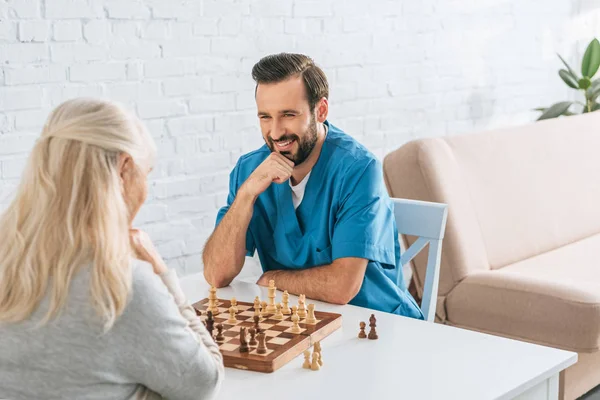 Senior mujer jugando ajedrez con sonriente joven asistente social - foto de stock