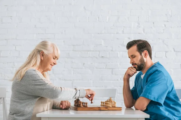 Side view of young male social worker playing chess with senior woman — Stock Photo
