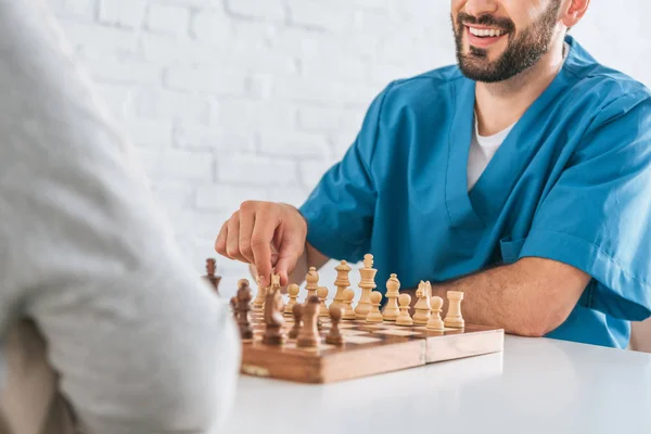 Plan recadré de travailleur social souriant jouant aux échecs avec une femme âgée — Photo de stock