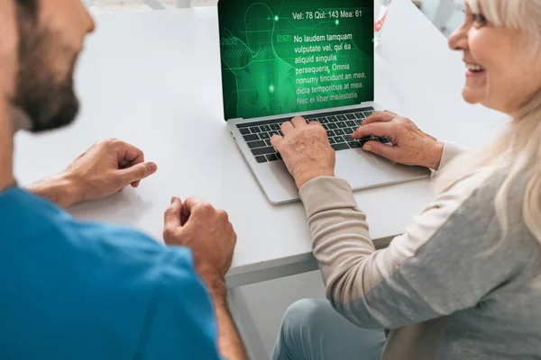 Cropped shot of young man and smiling senior woman using laptop — Stock Photo