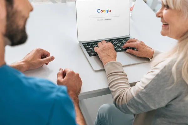 Обрезанный снимок молодого человека и улыбающаяся пожилая женщина с помощью ноутбука с веб-сайта Google на экране — стоковое фото