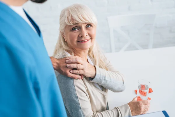 Sorridente donna anziana che prende la medicina e si tiene per mano di caregiver — Foto stock