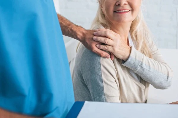 Schnappschuss von Sozialarbeiterin mit Klemmbrett und lächelnder Seniorin beim Händchenhalten — Stockfoto