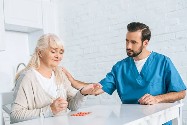 Sozialarbeiterin sieht lächelnde Seniorin beim Einnehmen von Medikamenten — Stockfoto