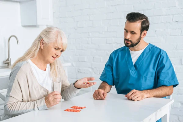 Caregiver looking at diseased senior woman taking medicine — Stock Photo