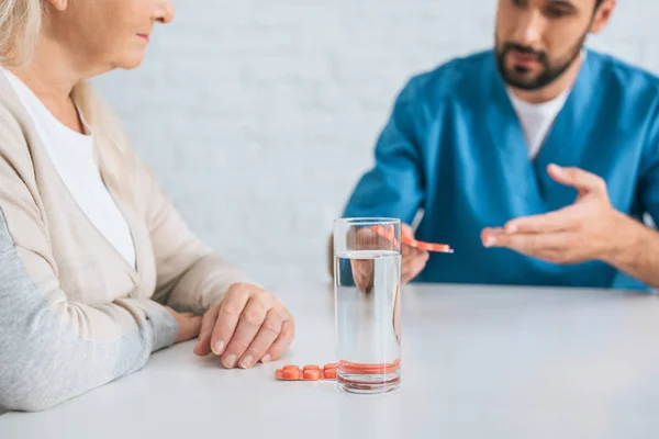 Cropped shot of male nurse giving pills to senior woman — Stock Photo