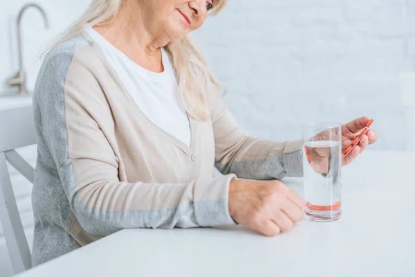 Schnappschuss von Seniorin, die am Tisch sitzt und Tabletten in der Hand hält — Stockfoto