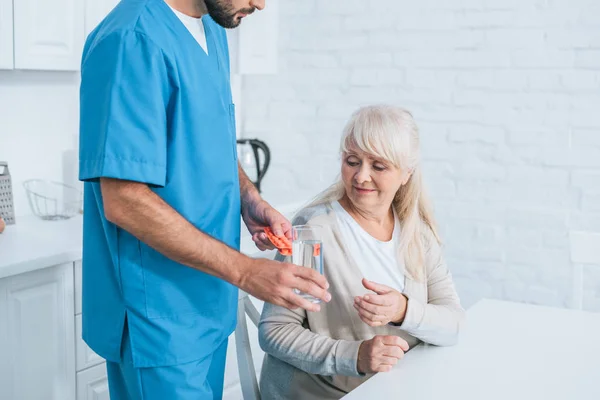 Cropped shot of social worker giving glass of water and pills to senior woman — Stock Photo