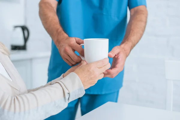 Cropped shot of caregiver giving cup of hot beverage to senior woman — Stock Photo