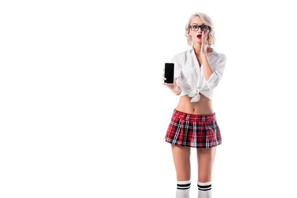 Shocked woman in seductive schoolgirl clothing showing smartphone with blank screen isolated on white — Stock Photo