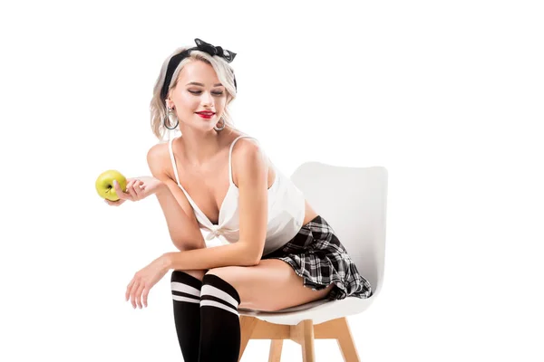 Young sexy woman in short plaid skirt and knee socks with apple in hand sitting on chair isolated on white — Stock Photo