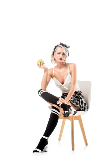 Young sexy woman in short plaid skirt and knee socks with apple in hand sitting on chair isolated on white — Stock Photo