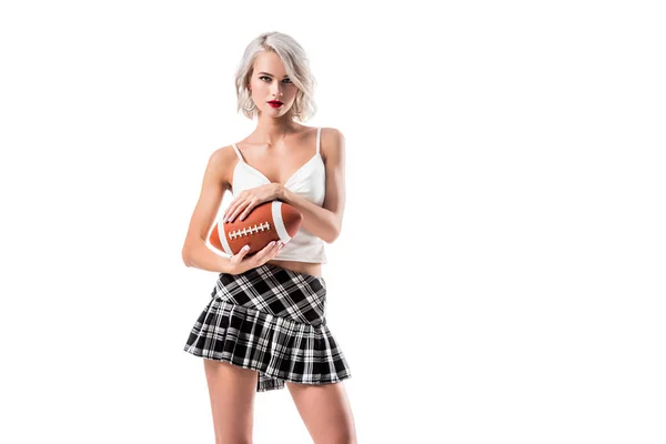 Ritratto di attraente donna bionda in breve plaid gonna studentessa tenendo palla da rugby isolato su bianco — Foto stock