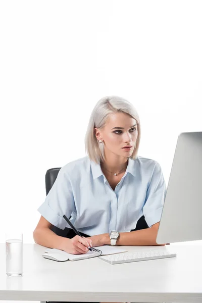 Retrato de empresaria enfocada que trabaja en el lugar de trabajo con vaso de agua, cuaderno y pantalla de computadora aislada en blanco - foto de stock