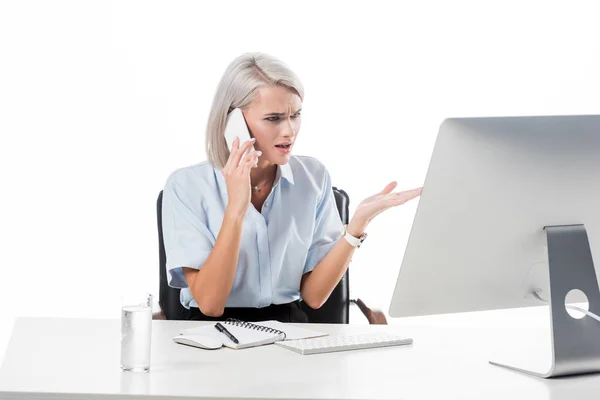 Retrato de la mujer de negocios hablando en el teléfono inteligente en el lugar de trabajo con un vaso de agua, portátil y pantalla de ordenador aislado en blanco - foto de stock