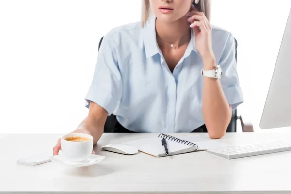 Partial view of businesswoman with cup of coffee at workplace with notebook and computer screen isolated on white — Stock Photo