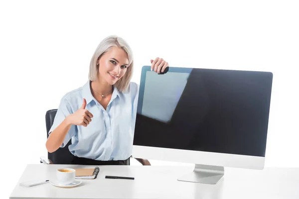 Портрет усміхненої бізнес-леді, що показує великий палець на робочому місці з порожнім екраном комп'ютера ізольовано на білому — стокове фото