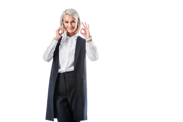 Портрет улыбающейся деловой женщины показывая знак ОК во время разговора на смартфоне изолированы на белом — стоковое фото
