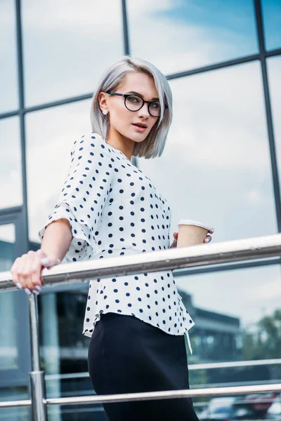 Mujer de negocios con estilo en gafas con café para ir en la mano en la calle - foto de stock