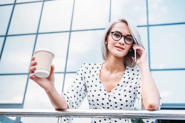 Portrait de femme d'affaires attrayante avec du café pour aller de pair parler sur smartphone dans la rue — Photo de stock