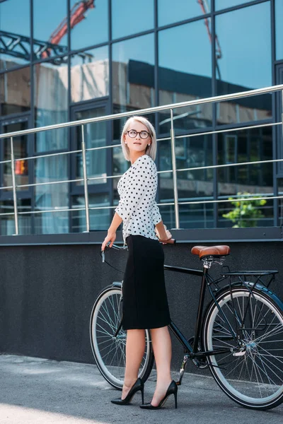 Jeune femme d'affaires dans des vêtements élégants avec vélo rétro debout sur la rue — Photo de stock